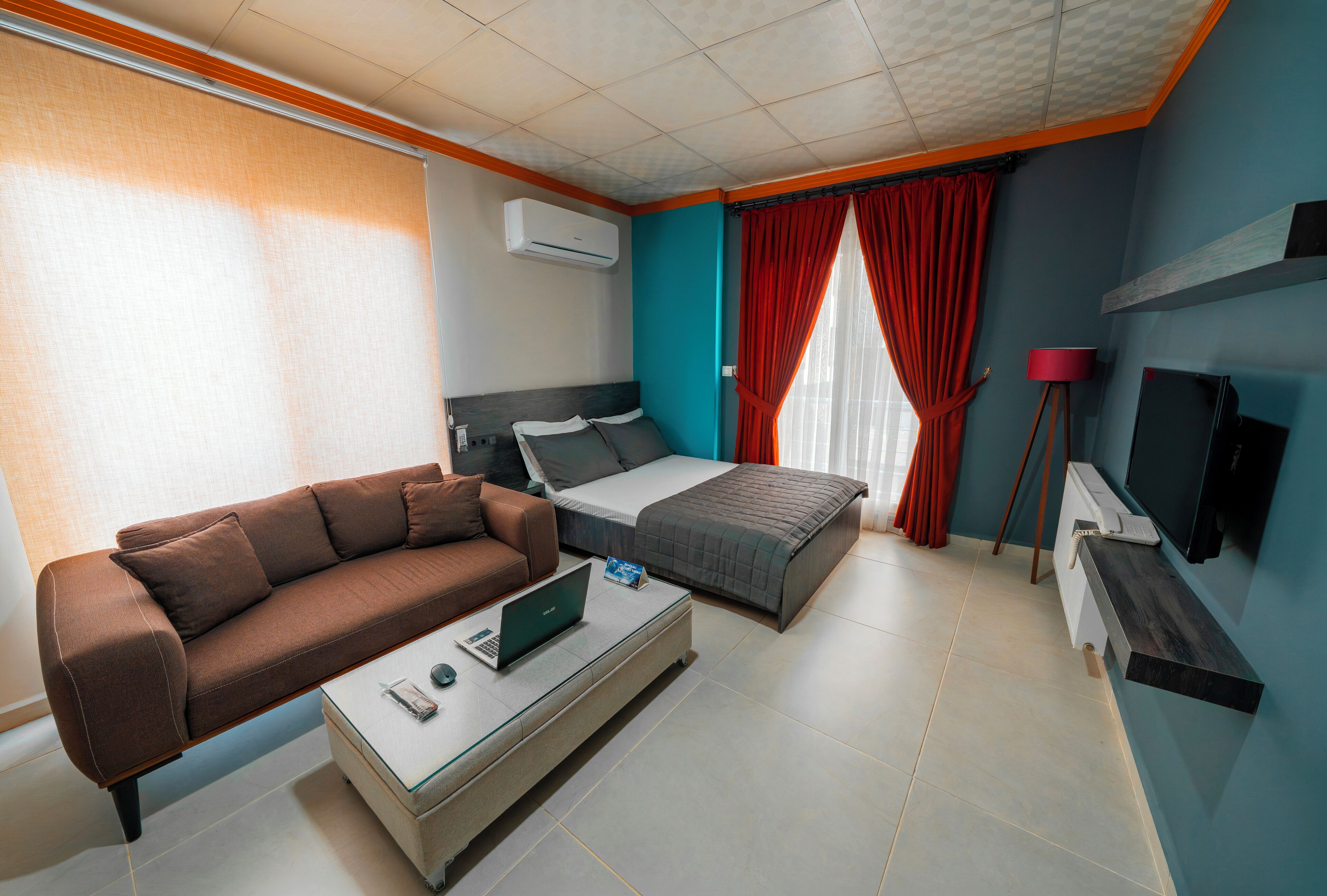Una habitación de hotel moderna con sofá, cama, escritorio y laptop, además de un televisor.