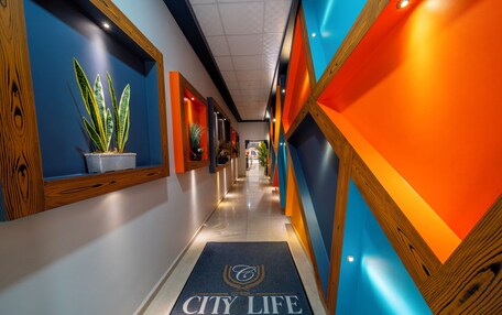 A hotel corridor with a blue and orange color scheme, potted plants, and a 'City Life Exclusive' carpet.