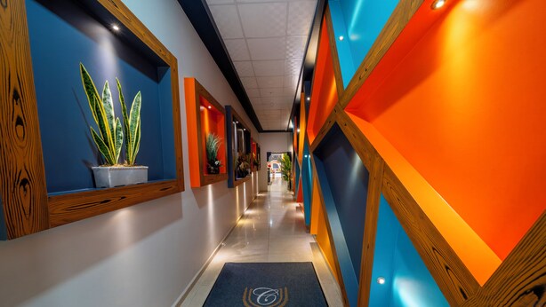 A hotel corridor with a blue and orange color scheme, potted plants, and a 'City Life Exclusive' carpet. - City Life (Iskenderun)
