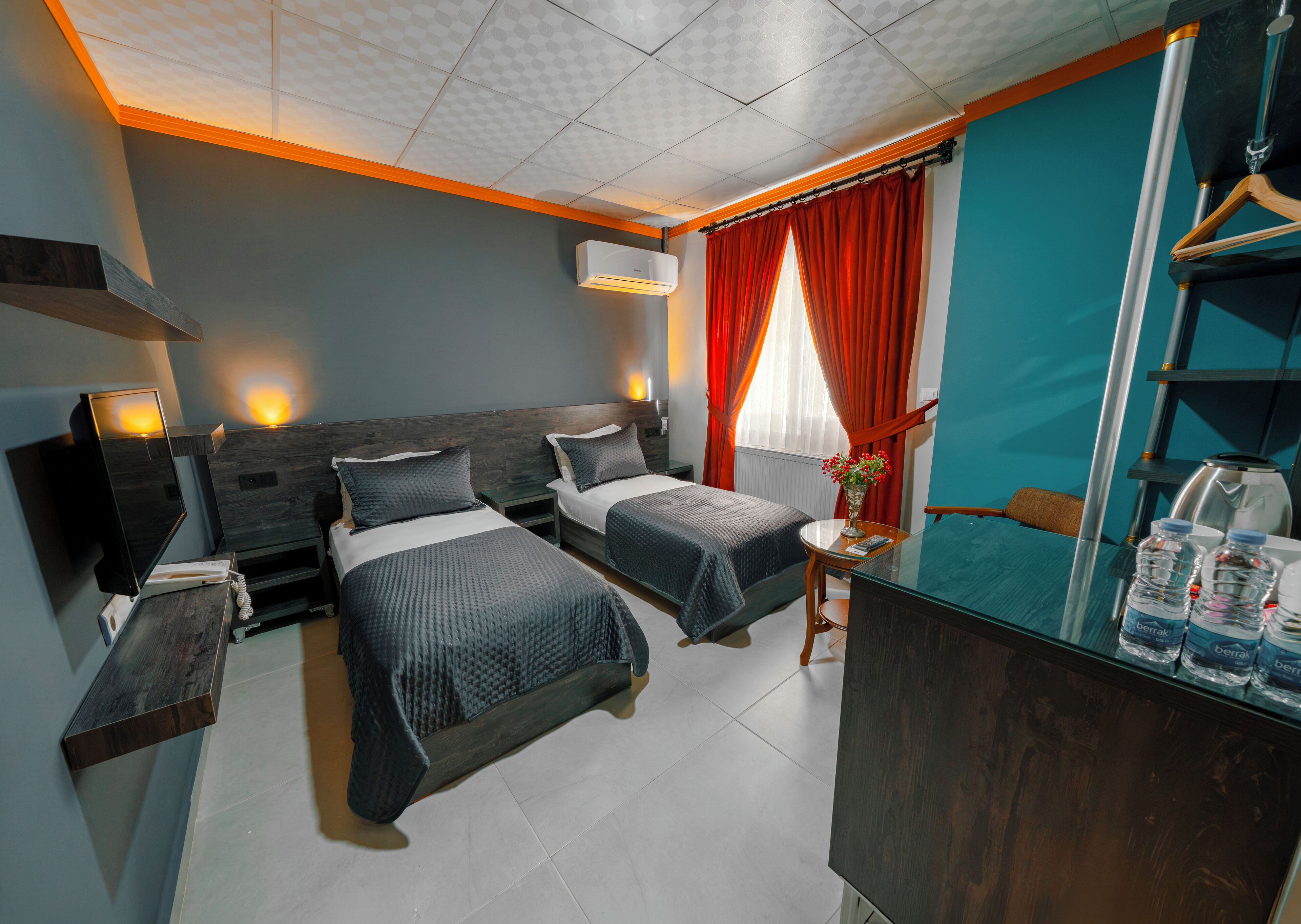 A hotel room with two beds, a mirror, a small table, and a water dispenser.