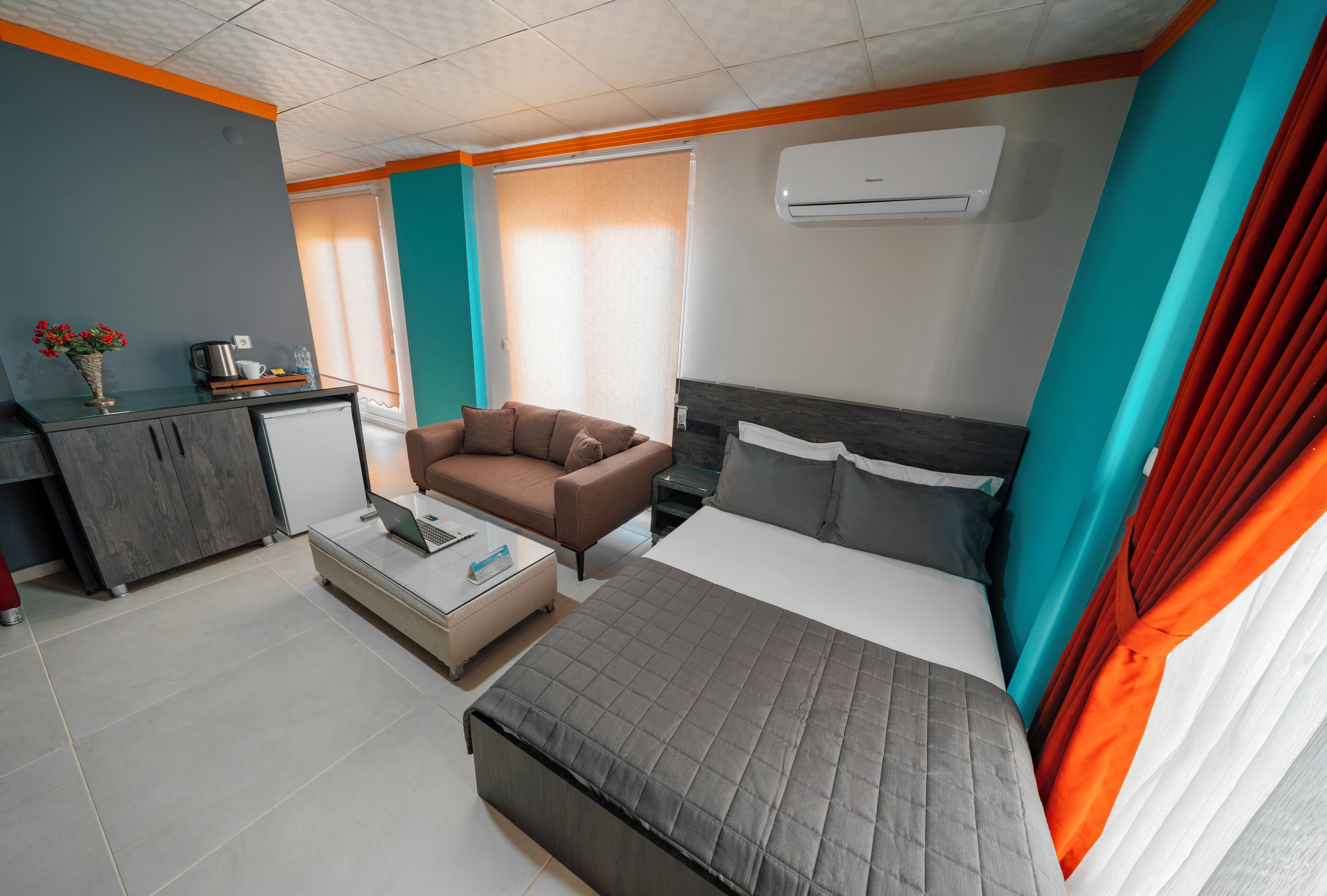 A modern hotel room with a bed, a sofa, a desk, and a kitchenette.