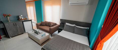 A modern hotel room with a bed, a sofa, a desk, and a kitchenette.