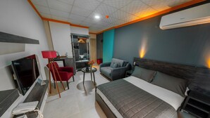 A modern hotel room with a bed, a desk, a chair, a TV, and an air conditioning unit. - City Life (Iskenderun)