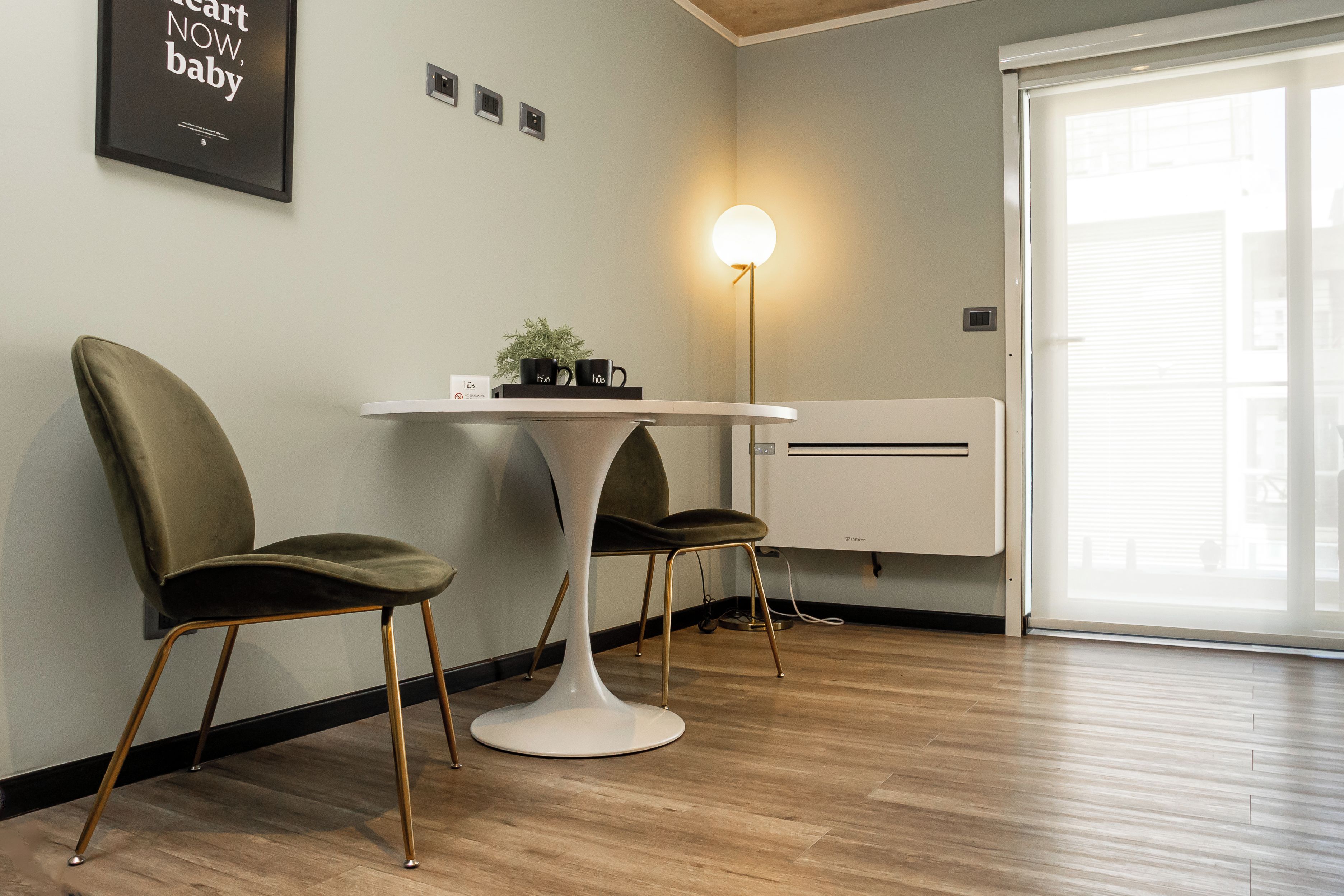 A modern room with a round table, two chairs, a floor lamp, a wall-mounted air conditioner, and a window with blinds.