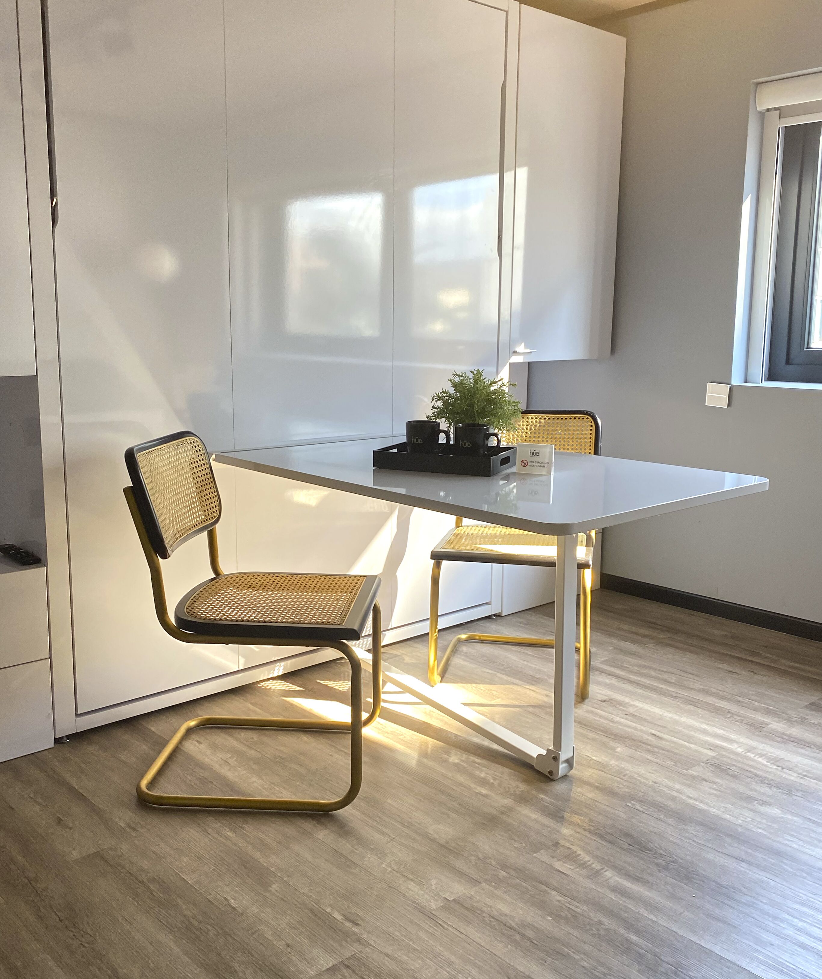 A modern kitchen with a white table, two wicker chairs, and a small potted plant.