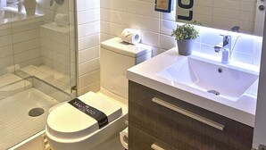 Un baño moderno con cabina de ducha de vidrio, inodoro, lavamanos con espejo y toallero.