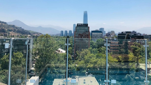 Un paisaje urbano con edificios modernos, incluyendo un rascacielos destacado, y vistas de montañas al fondo.