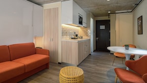 Un espacio habitable compacto con kitchenette, un sofá, una mesa de comedor con sillas y una pequeña mesa redonda con una planta.