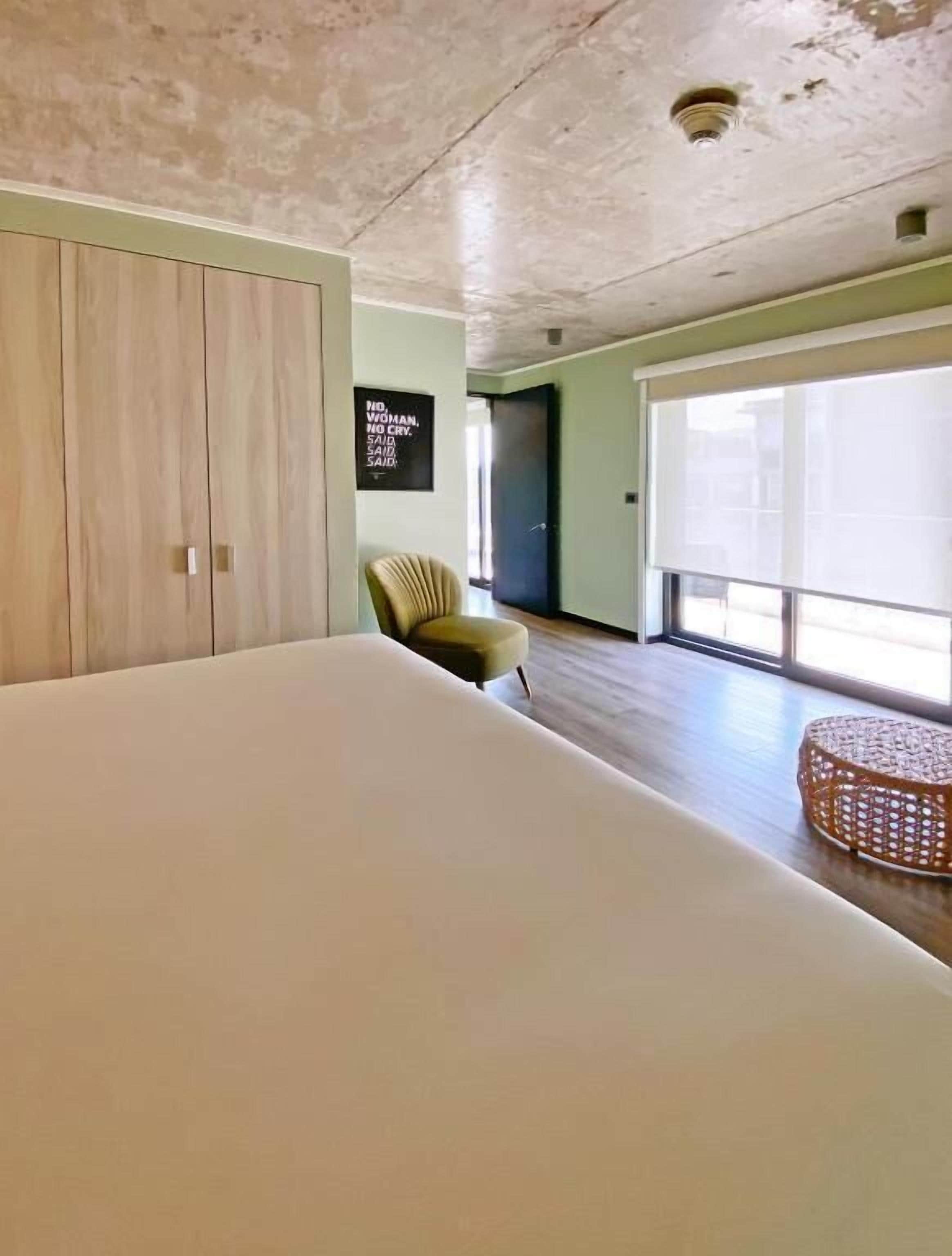 A bedroom with a large bed, a chair, a wall-mounted TV, and a window.
