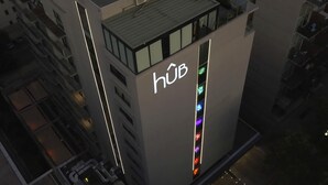 Un edificio moderno con un llamativo letrero 'hüb' en el costado, que presenta una tira de luz vertical con varios colores.