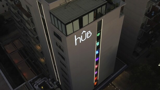 Un edificio moderno con un llamativo letrero 'hüb' en el costado, que presenta una tira de luz vertical con varios colores.