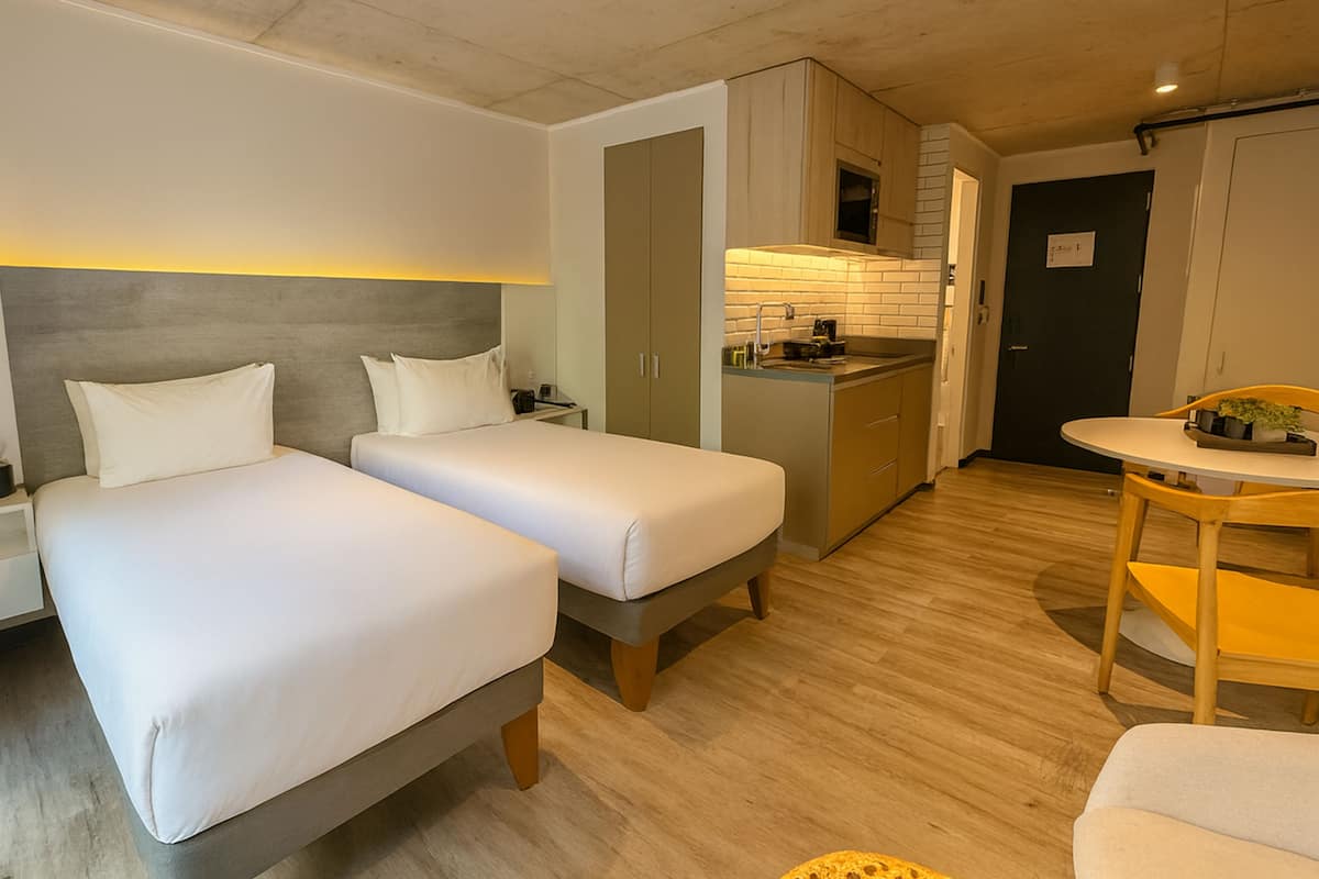 Una habitación de hotel compacta con dos camas individuales, un kitchenette pequeño y una zona de comedor.