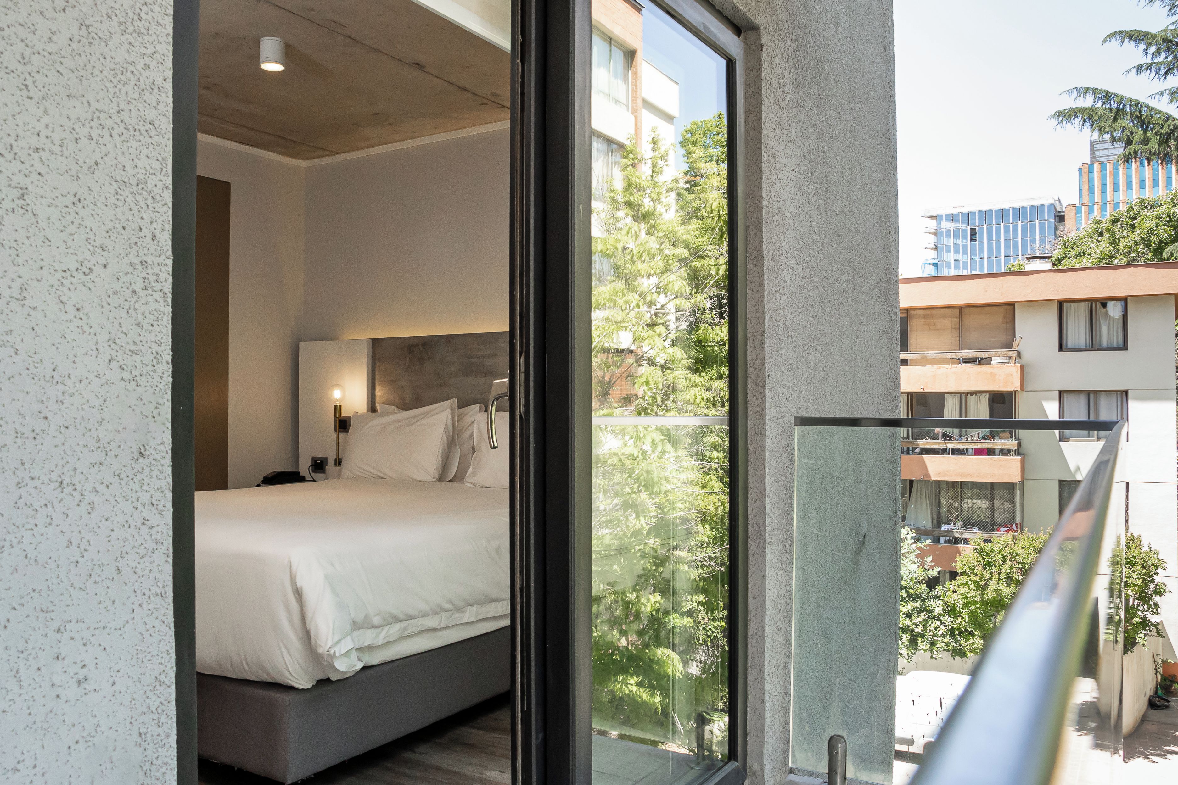 Un dormitorio moderno con una cama grande, una mesita de noche y una ventana con vistas a un paisaje urbano.