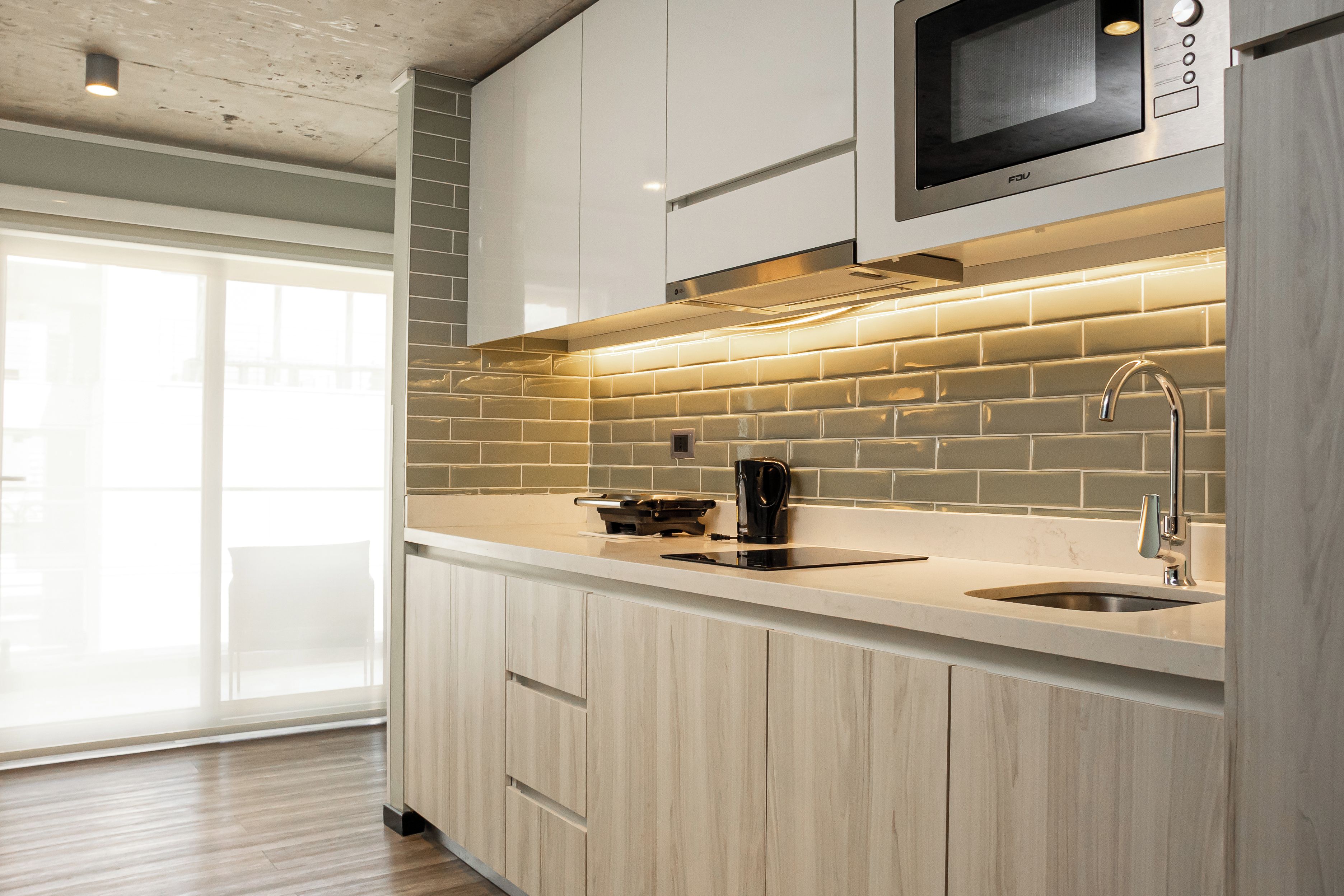 A modern kitchen with a microwave, kettle, and stainless steel sink.