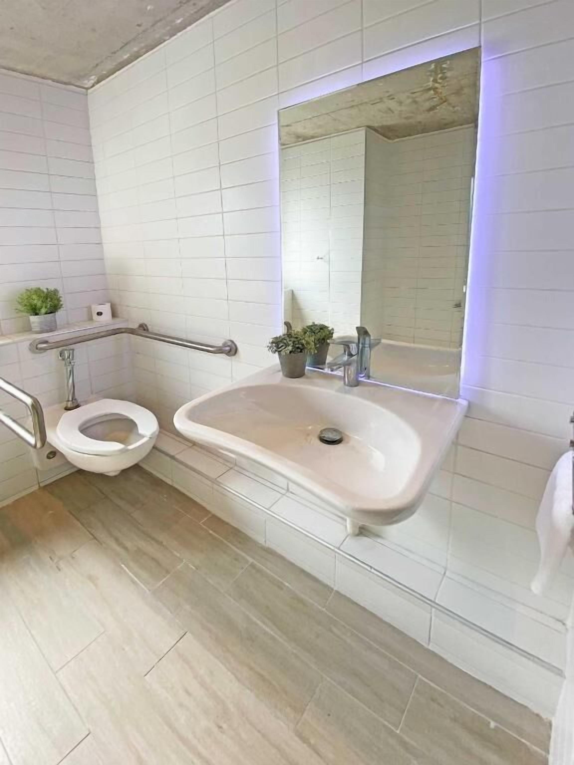A modern bathroom with a white sink, a toilet, and a mirror with LED lighting.