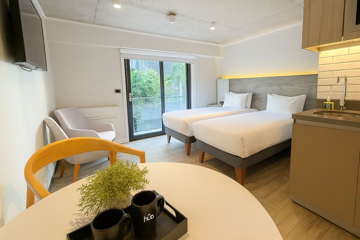 A modern hotel room with a bed, a desk, a chair, a TV, and a bathroom.