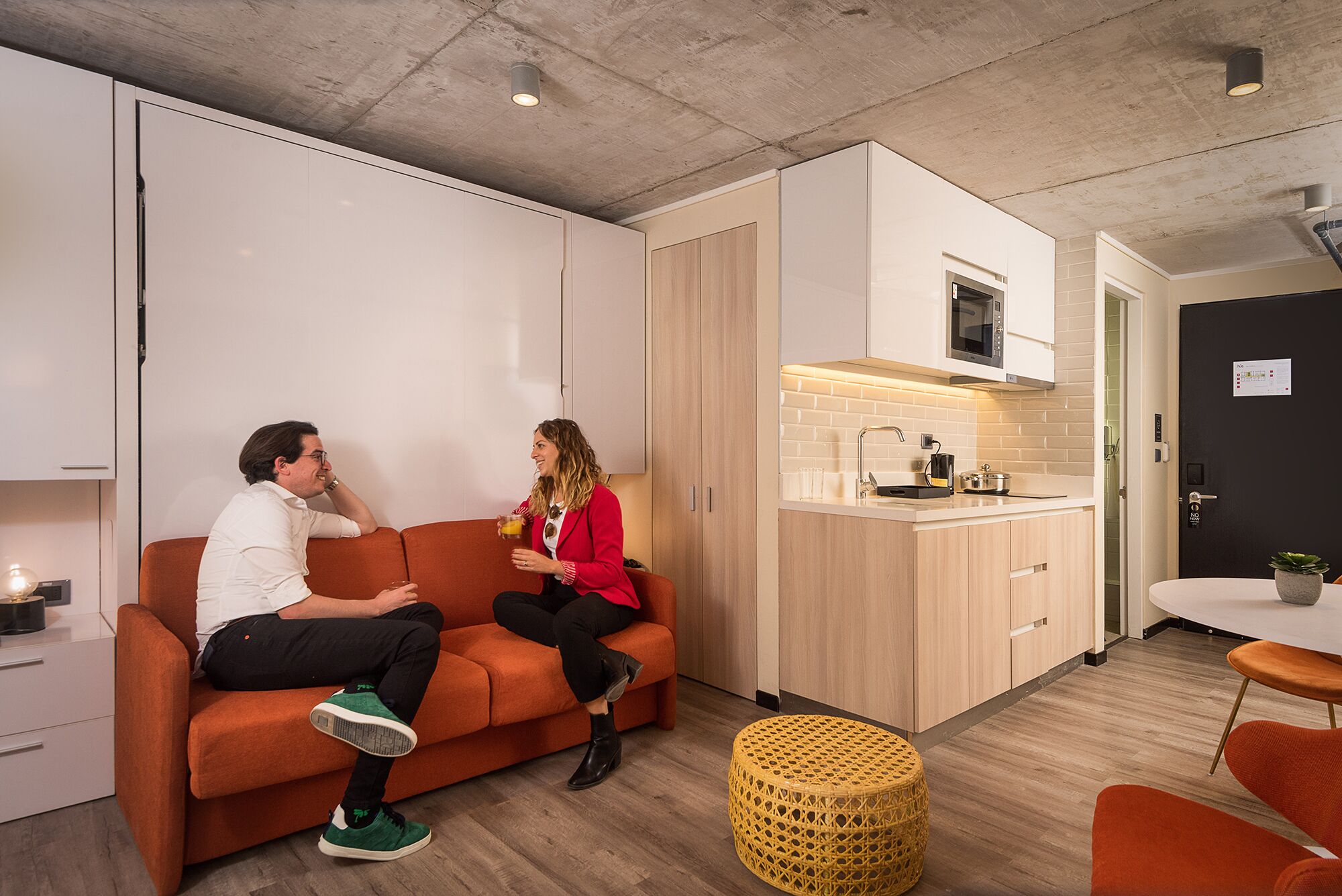 Una sala moderna con un sofá, una zona de cocina con microondas y una mesa de comedor.