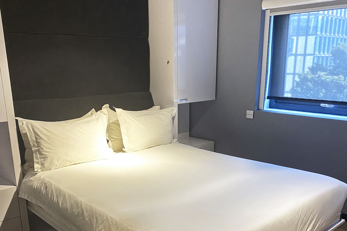 Un dormitorio moderno con cama, cabecero, ventana y suelo de madera.