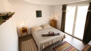 Quarto com cama, mesas de cabeceira, cômoda e janela com cortinas.