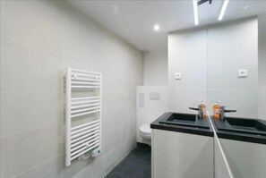 Een moderne badkamer met een betegelde muur, een witte radiator, een toilet en een zwarte wastafel met twee zeepdispensers.