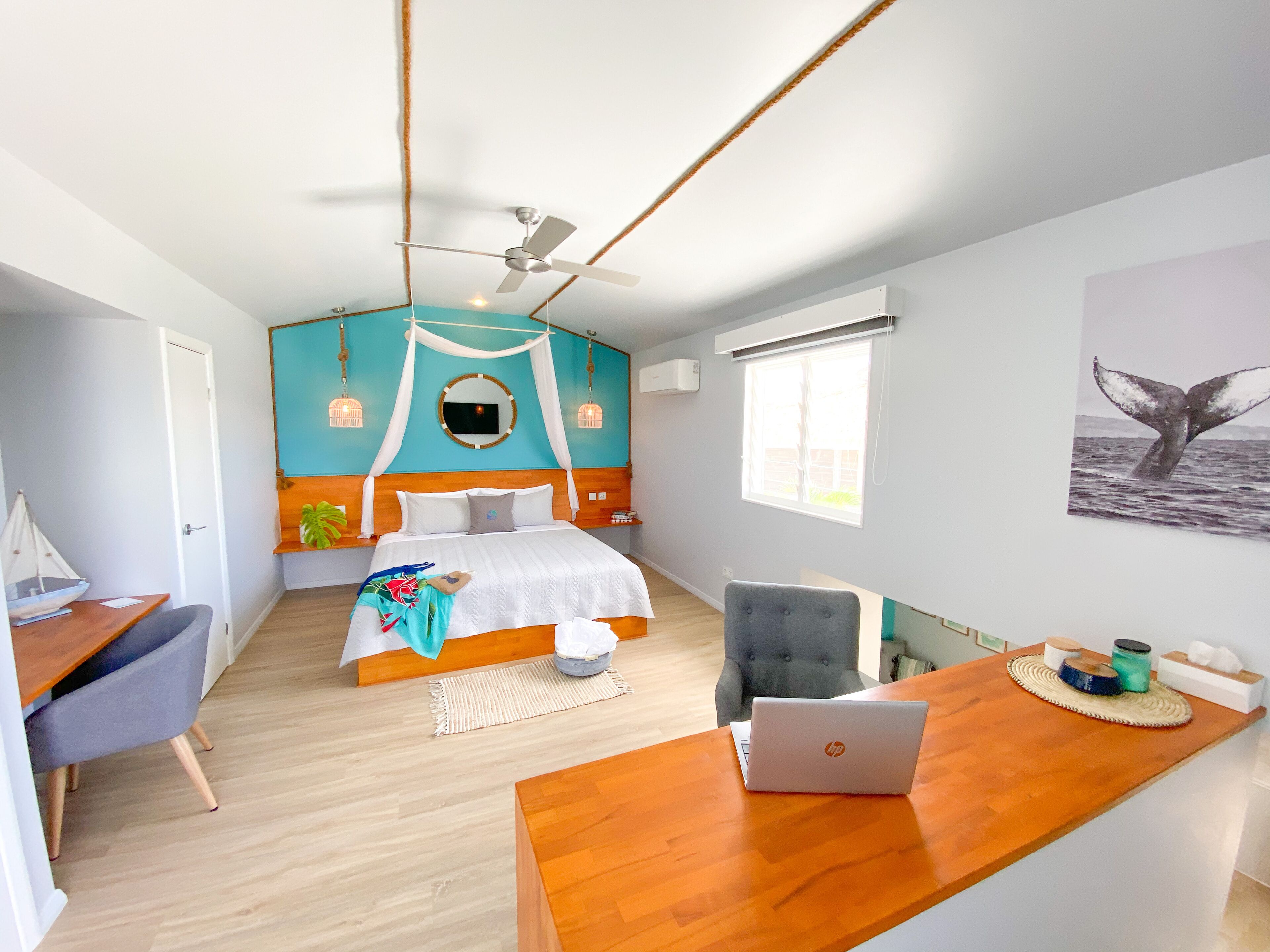 A bedroom with a bed, a desk with a laptop, a chair, a window, and a wall-mounted air conditioner.