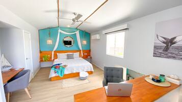 A bedroom with a bed, a desk with a laptop, a chair, a window, and a wall-mounted air conditioner.