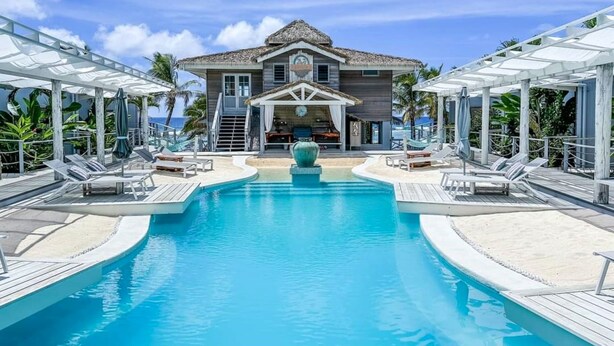 Un resort con una grande piscina, sdraio e un edificio con tetto di paglia.