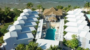 Una vista aerea di un resort con una piscina centrale, diversi edifici in stile bungalow e vista sulla spiaggia.