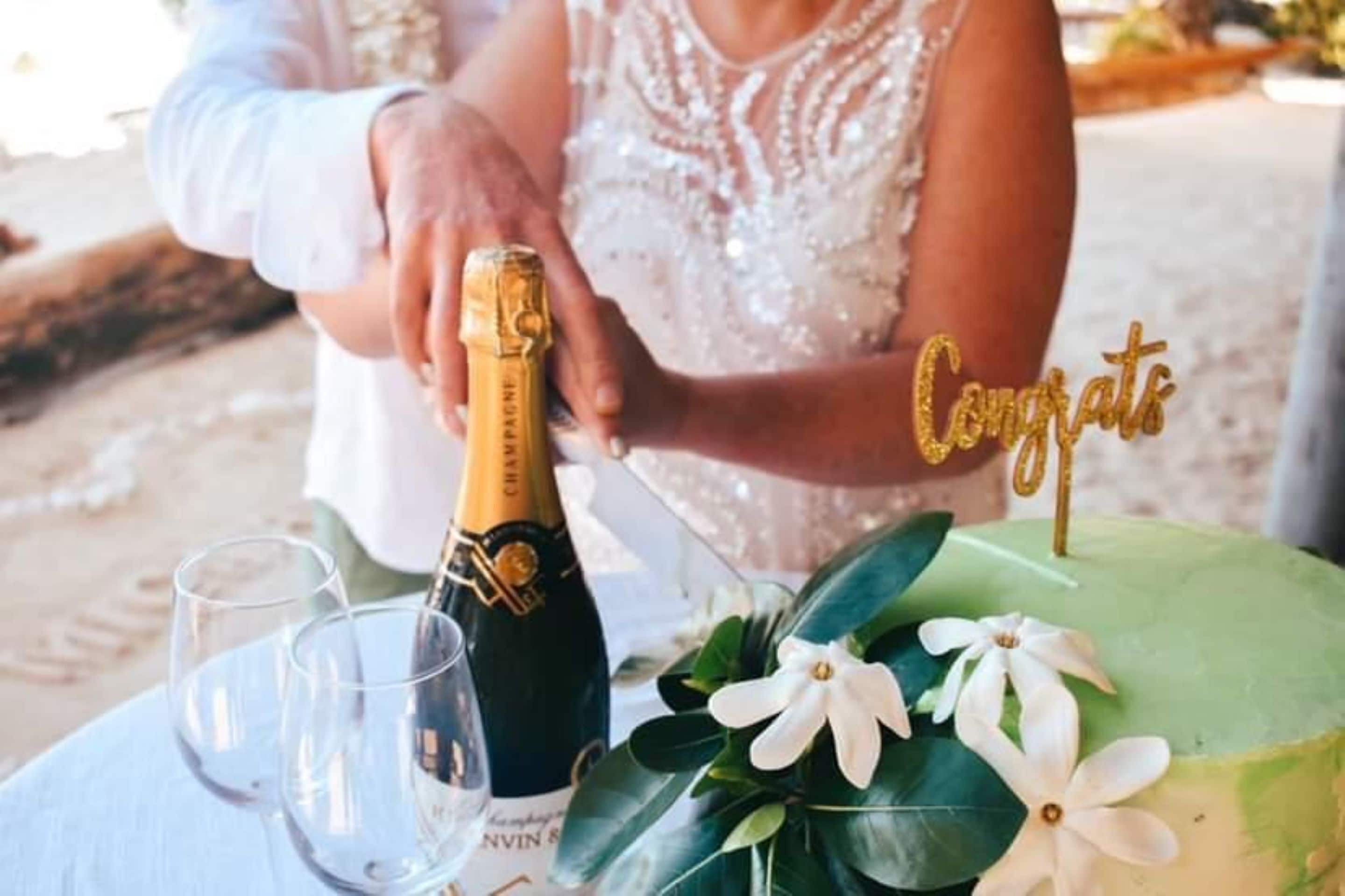 Un pastel de bodas con un adorno que dice 'Felicidades', una botella de champán y copas sobre una mesa.
