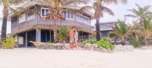 A beachfront property with a thatched-roof structure, palm trees, and a sandy beach.