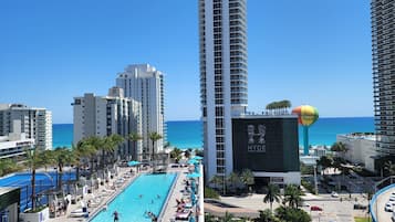 A high-rise hotel with a rooftop pool area, palm trees, and a view of the ocean.