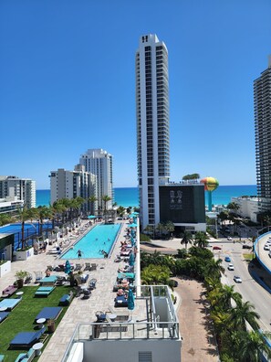 A high-rise hotel with a rooftop pool area, palm trees, and a view of the ocean.