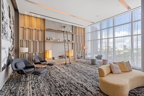 A modern living room with a large window, a sofa, two armchairs, a coffee table, and a bookshelf.