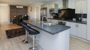 A modern kitchen with a central island, stainless steel appliances, and a dining area with bar stools. - Te Awa Napier Treasure - Napier Holiday Home (Napier City)