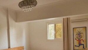 Un dormitorio con cama de madera, candelabro, ventana con cortinas y un cuadro en la pared.