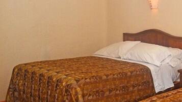 A room with two beds, each with patterned bedding, a wall-mounted light fixture, and a framed picture on the wall.