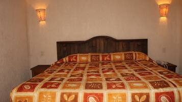 Una cama con una colcha estampada, dos lámparas de pared y un cabecero de madera.