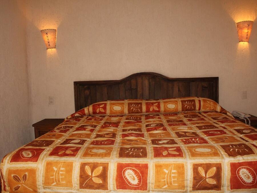 Una cama con una colcha estampada, dos lámparas de pared y un cabecero de madera.