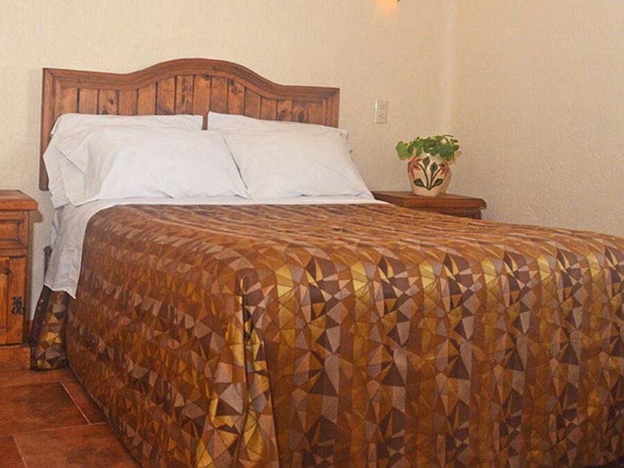 Une chambre à coucher avec une tête de lit en bois, une couvre-lit à motifs, une table de chevet avec un téléphone et une plante en pot.