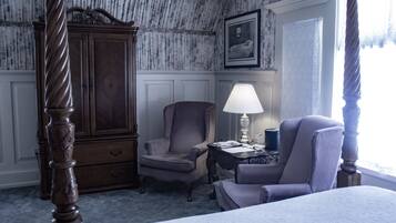 Une chambre à coucher avec un lit à baldaquin, une armoire en bois, deux fauteuils, une table de chevet avec une lampe et un tableau encadré au mur.