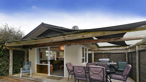 A covered patio with a wooden deck, a table with chairs, and a grill. - Blue Lagoon - Kaiteriteri Holiday Unit (Kaiteriteri)