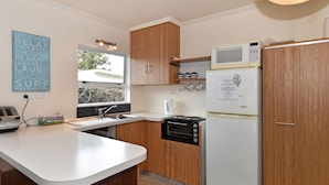 A compact kitchen with wooden cabinets, a white countertop, a built-in oven, a microwave, and a refrigerator. - Blue Lagoon - Kaiteriteri Holiday Unit (Kaiteriteri)