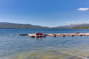 A calm lake with a dock extending into the water, surrounded by mountains and dense forests. - Lakefront condo w/ beach and seasonal heated pool (Mccall)