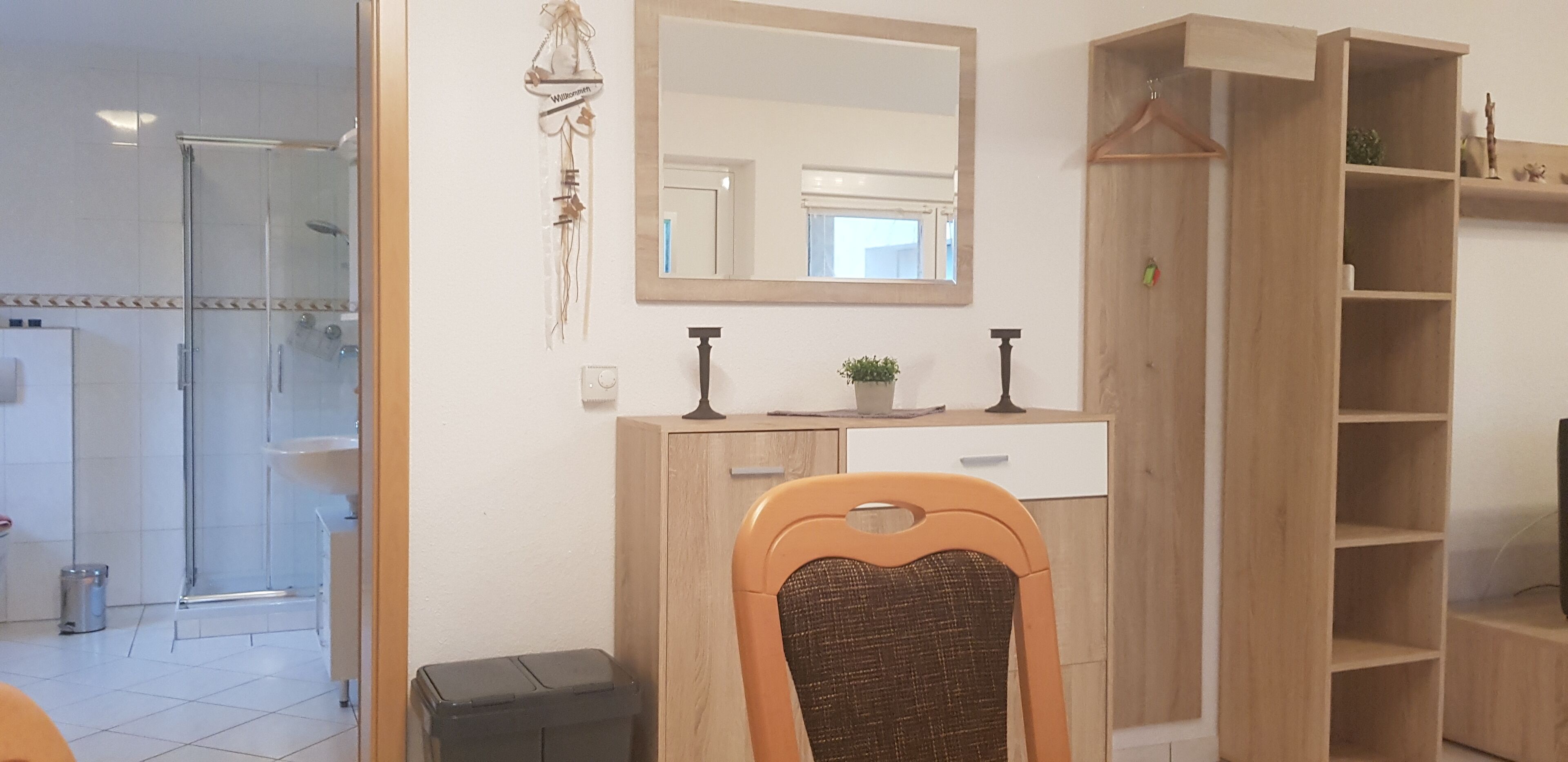 A bathroom with a glass shower enclosure, a wooden vanity with a mirror, and a shelf with decorative items.
