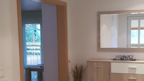 Une pièce avec un sol carrelé, un meuble en bois doté de tiroirs, un miroir au mur et une porte donnant sur une autre pièce.