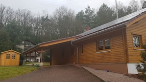 Une cabane en bois avec un porche couvert, un petit abri de jardin et une allée gravillonnée.