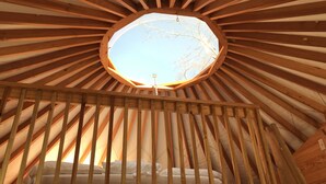A circular skylight in a wooden room with a bed and slatted ceiling.