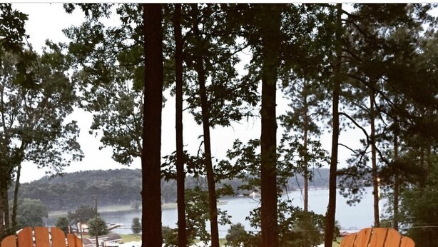Two Adirondack chairs facing a campfire with a lake and forest in the background.