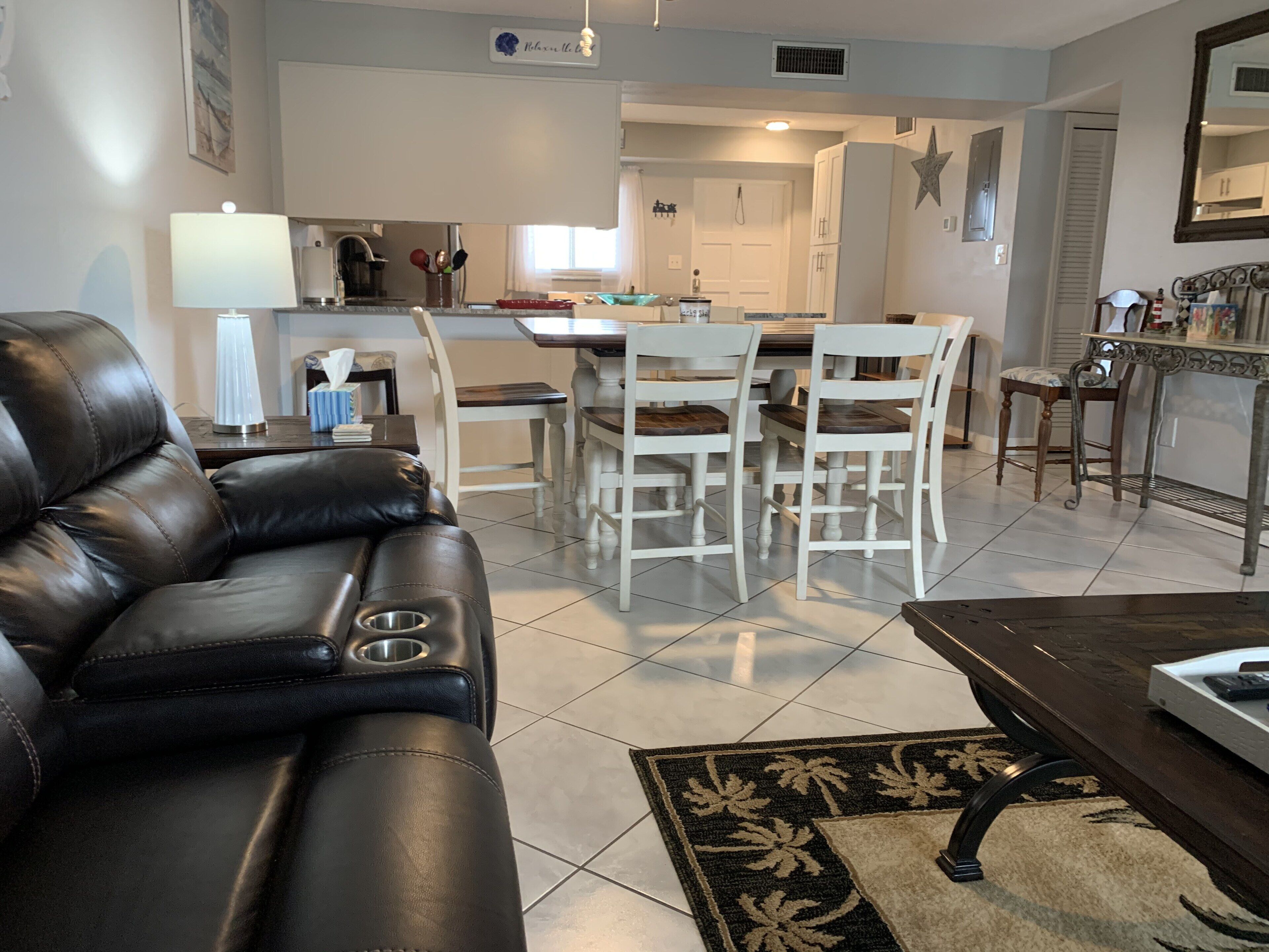 Un salon moderne avec un canapé en cuir, un coin repas avec des chaises blanches et une cuisine en arrière-plan.