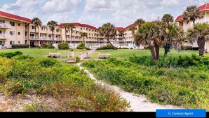 A hotel with multiple buildings, a central courtyard with palm trees, and a pathway leading to the entrance. - Beachfront condo with direct pool & ocean view on St Augustine Beach (St Augustine Beach)